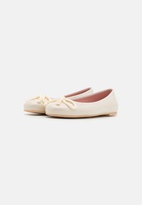 Bailarinas em couro creme com uma textura suave, apresentando um detalhe de corda atada na ponta e uma sola baixa bege.