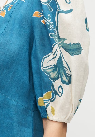 Μανίκι από μπλε και λευκό ύφασμα με λουλουδένια σχέδια σε πράσινο, κίτρινο και πορτοκαλί σε σούρες με ελαστικό μανσέτα.