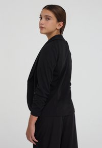 Blazer nero con maniche lunghe, apertura frontale e texture liscia. Presenta una vestibilità tailored e un sottile accento sulle spalle.