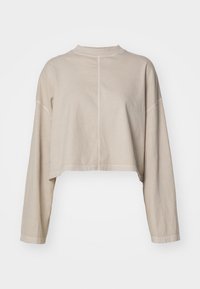 Beige lyhyempi pitkähihaisen collegepaita, jossa on pieni korkea kaulus ja näkyvät keskisaumat etu- ja takapuolella.