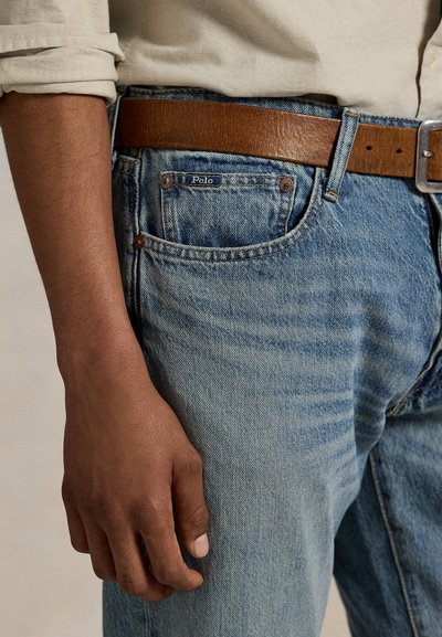 Calças de ganga azul claro, com um design clássico de cinco bolsos. Acompanhadas por um cinto de couro castanho com uma fivela prateada.