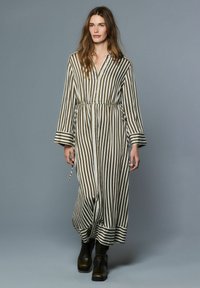 Pruhované šaty s dlouhým rukávem v olivově zelené a bílé barvě s knoflíkovou légou a zavazováním v pase, doplněné černými kotníkovými botami.