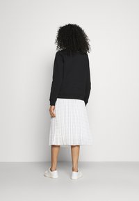 Sudadera negra de manga larga, llevada sobre una falda blanca con pliegues que presenta rayas verticales. Zapatillas blancas completan el conjunto.