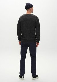 Dunkelgrauer Strickpullover mit Rippbündchen und Saum, kombiniert mit marineblauen Hosen und schwarzen Sneakers. Mann trägt eine marineblaue Mütze, von hinten betrachtet.
