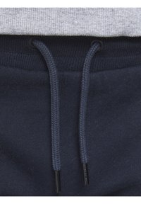 Námořnické tepláky s pružným pasem a pletenými šňůrkami. Na vrchu je šedá, texturovaná látka s žebrovaným vzorem.