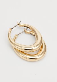 Et par skinnende gullfargede tykke hoops med lås, lagt overlappende på en hvit bakgrunn.