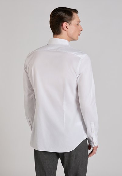 Camisa blanca de manga larga con corte recto, puños abotonados y cuello clásico, exhibida sobre un fondo neutro.