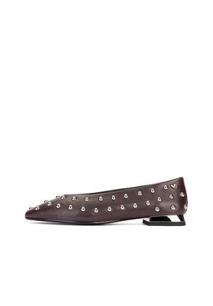 Zapato plano marrón oscuro con puntera puntiaguda, decorado con tachuelas plateadas espaciadas de manera uniforme y un tacón metálico geométrico bajo.