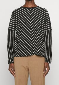 Svetr s černobílými pruhy a zigzagovým vzorem, dlouhými rukávy, kulatým výstřihem a volným střihem. Nosit s béžovými kalhotami.