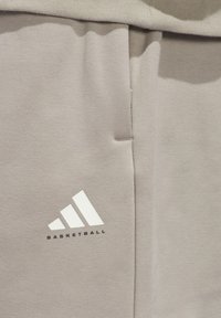 Graue Sporthose aus weichem Material, mit einem weißen Adidas-Logo und dem Text "BASKETBALL" sowie seitlichen Taschen für zusätzlichen Nutzen.