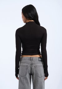 Long-sleeve, black top with a fitted design, smooth texture, and high collar. Paired with gray wide-leg jeans featuring rear pockets.