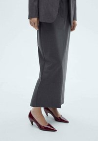 Pantofi cu toc din piele patent roșie, cu vârf ascuțit și toc conic mic, asortați cu pantaloni gri cu picior larg și un sacou corespunzător.