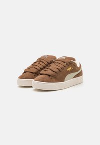 Brown suede sneakers with a textured off-white sole, featuring beige accents, lace-up design, and a small logo on the side.