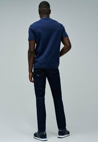 Camiseta de manga corta en azul marino con cuello redondo, combinada con jeans de mezclilla azul oscuro y zapatillas marinas. Diseño simple y casual sin patrones.