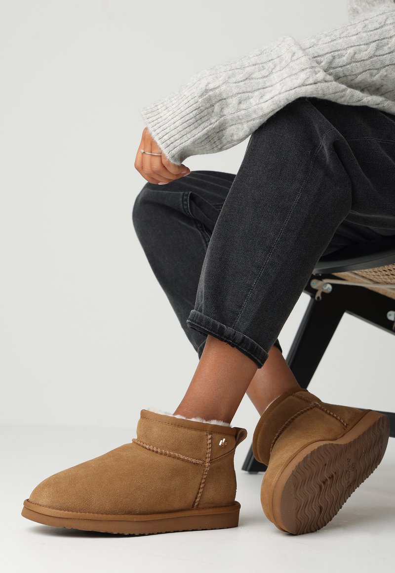 Bottines en daim marron avec une doublure intérieure douce, dotées d'un design bas et d'une semelle texturée. Associées à un jean foncé et un pull léger.