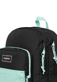 Zaino nero con accenti verde menta, dotato di una tasca frontale testurizzata con rete e chiusure a zip. Inclusi spallacci imbottiti e maniglia superiore.