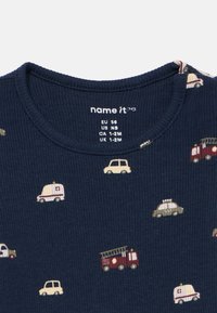 Ναυτικό ριγέ μπλουζάκι με πολύχρωμα σχέδια οχημάτων, συμπεριλαμβανομένων ενός πυροσβεστικού οχήματος, ενός αυτοκινήτου και ενός τροχόσπιτου. Διαθέτει στρογγυλή λαιμόκοψη και ριγέ υφή.