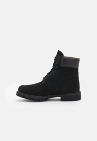 Botas de tobillo de ante negro con un collar acolchado, cierre de cordones en la parte delantera y una suela de goma resistente. Presentan paneles texturizados para un detalle adicional.