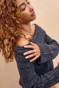 Pulover gri cu dungi, supradimensionat, cu un guler larg, textură moale. Modelul poartă un colier din aur și un inel din aur, evidențiind unghiile decorative.