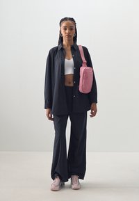 Svart oversized skjorte, hvit crop topp, svarte bukser. Rosa crossbody-veske, lyserosa sneakers. Glatt stoff, avslappet passform og uformelt design.