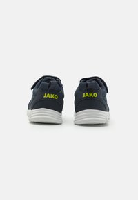 Baskets de sport bleu marine avec une tige en mesh, une sangle Velcro et une semelle blanche ; présente le logo "JAKO" en jaune fluo sur les talons.