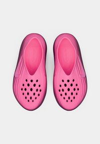 Pár svetloružových klzákov z peny s perforovanými otvormi na vrchu a diskrétnym logom Nike na boku, zobrazené zhora.