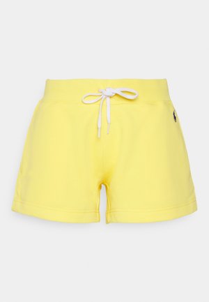 Gelbe Freizeithose mit weißem Kordelzugbund und kleinem dunklem Logo an der rechten Hüfte, vor einfarbigem Hintergrund dargestellt.