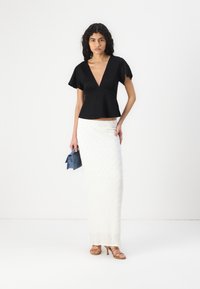 Čierny peplum top s krátkymi flutter rukávmi a hlbokým V-výstrihom. Biela textúrovaná dlhá sukňa s priliehavou siluetou. Modrý clutch a nahé podpätky.