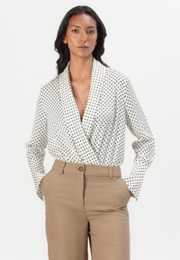 Hvit prikkete omslagsbluse med lange ermer, dyp V-hals og en glatt tekstur, sammen med beige høyt liv bukser.
