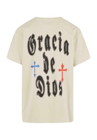 Camiseta de algodón crema con el texto negro "Gracia de Dios", con cruces rojas y azules que acentúan el diseño. Manga corta y corte relajado.