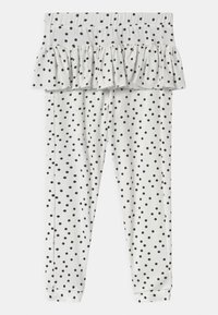 Białe legginsy dla niemowląt w czarne kropki, z przymocowaną falbaną na pasku.