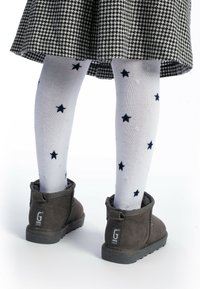 Botines de gamuza gris con suelas texturizadas, usados sobre medias blancas con patrones de estrellas en azul marino, combinados con una falda de pata de gallo en blanco y negro.