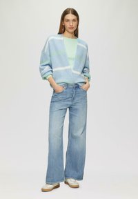 Gehaakte cardigan in lichtblauw met witte en groene strepen, gecombineerd met lichte wijde jeans en beige sneakers.