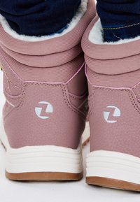 Rosa High-Top-Sneaker mit strukturiertem Finish, weißen Sohlen und grauen Logos. Weiches Futter, das oben sichtbar ist, und gestickte Akzente.