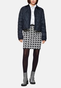 Navy quilted cropped jacket over a white button-up shirt, paired with a patterned black and white skirt and knee-high gray boots.