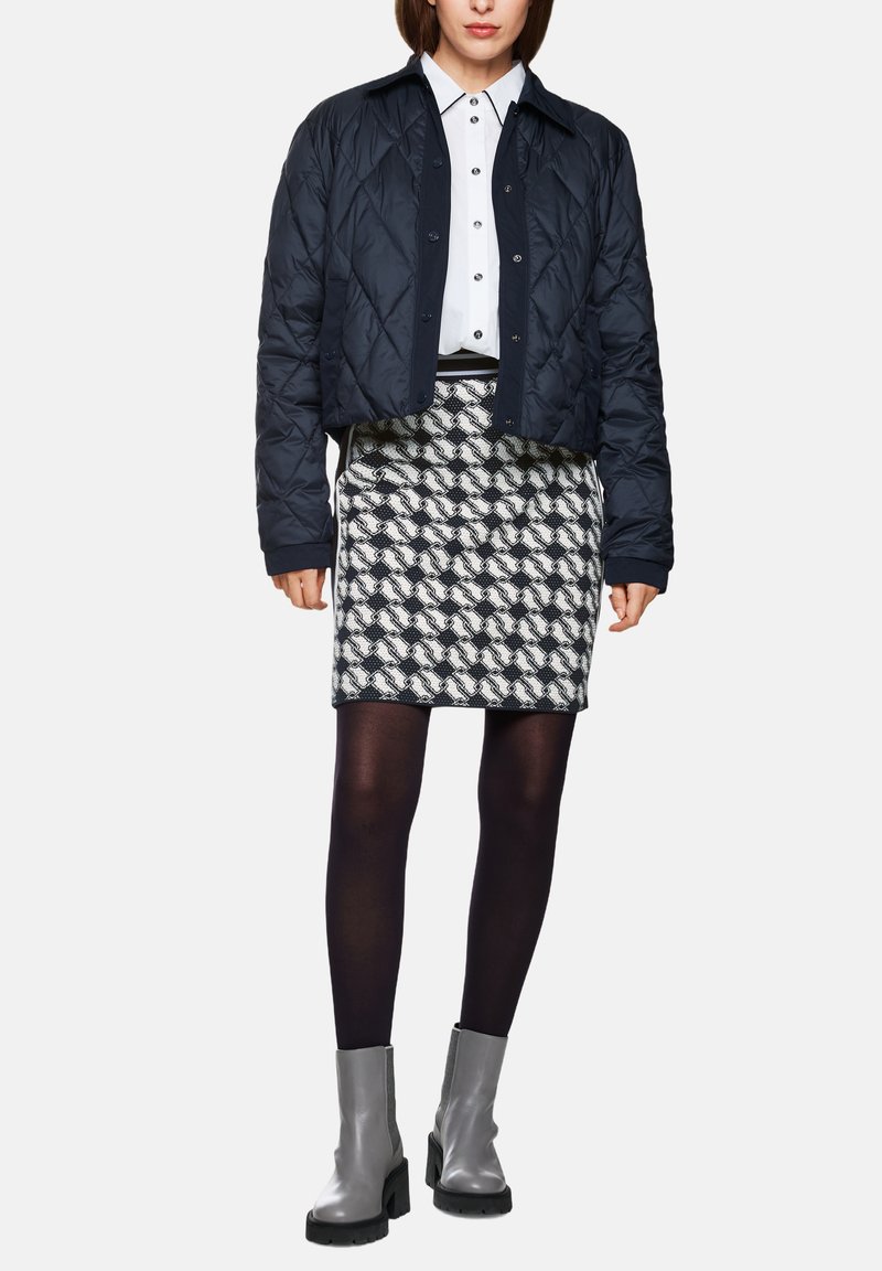 Navy quilted cropped jacket over a white button-up shirt, paired with a patterned black and white skirt and knee-high gray boots.