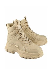Zapatillas altas beige hechas de lona y goma con suelas gruesas, cuello acolchado y acentos texturizados. Cintas y logo en la lengüeta.