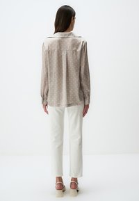 Blusa beige a pois con maniche lunghe e colletto, abbinata a pantaloni bianchi a gamba dritta e sandali con tacco a blocco color crema.