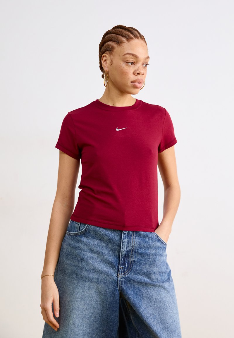 Burgundinė trumpa rankovė marškinė su apvalia iškirpte ir baltu Nike logotipu ant krūtinės, derinami su plačiais mėlynais džinsiniais šortais.