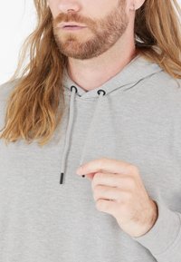 Szara, zapinana na kaptur bluza z miękką teksturą, sznurkiem do regulacji z czarnymi akcentami oraz luźnym krojem widocznym przy dekolcie.