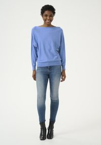 Lichtblauwe trui met een ruime halslijn en lange mouwen, gecombineerd met strakke blauwe jeans en zwarte enkellaarsjes. Makkelijke stoftextuur.