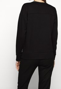 Sudadera negra de corte relajado, con cuello redondo y hombros caídos. Presenta una textura suave y un dobladillo y puños acanalados para un detalle adicional.