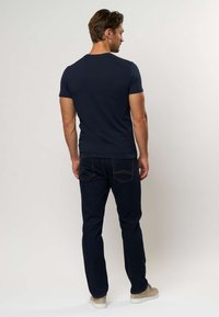 Tamsiai mėlyna trumpomis rankovėmis marškinėliai, derinami su tamsiais džinsais. Turi apvalų iškirptę ir laisvą prigludimą, dėvimi su šviesios spalvos batais.