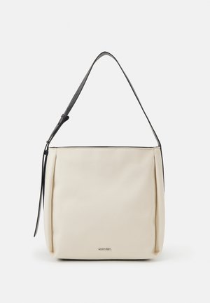 Sac à main rectangulaire crème avec bandoulière réglable noire et petit logo Calvin Klein au centre devant.