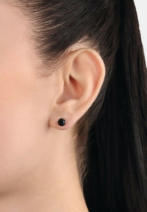 Pendientes de stud negros con un diseño esférico texturizado, colocados en la oreja de un modelo, enfatizando las líneas limpias y el tono de piel suave.