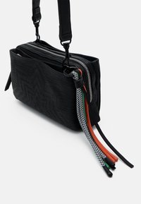 Schwarze strukturierte Handtasche mit doppeltem Reißverschluss, ausgestattet mit einem gemusterten Tragegurt mit grünen, orangefarbenen, roten und schwarzen Akzenten. Kompakte rechteckige Form.