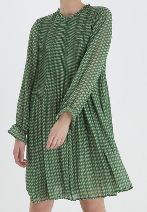 Grünes, plissiertes Kleid mit langen Ärmeln, rundem Ausschnitt und geometrischem Muster in verschiedenen Grüntönen und Weiß. Leichter Stoff, lockerer Schnitt.