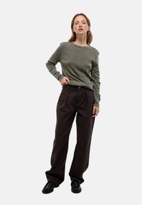 Pull en maille verte associé à un pantalon marron ample. Le pull a un col rond simple et des détails subtils aux épaules.