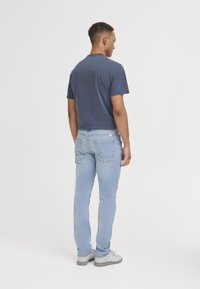 Tricou cu mânecă scurtă de culoare albastru închis pentru bărbați, blugi slim-fit de culoare albastră deschisă și adidași gri. Material neted cu un design casual, ajustat.