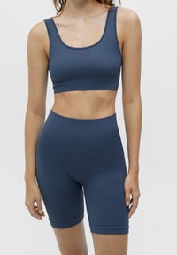 Modrý žebrovaný sportovní podprsenka a odpovídající cyklistické šortky, s hlubokým výstřihem, bezšvovým designem a elastickým materiálem pro pohodlí.